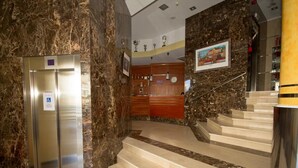 Un hall d’entrée au sol en marbre, avec un comptoir d’accueil, un escalier et un ascenseur.