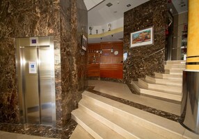 Un vestíbulo con suelo de mármol, una recepción, una escalera y un ascensor.
