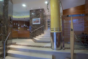 Un vestíbulo de hotel con paredes de mármol, una escalera y una mesa de recepción.