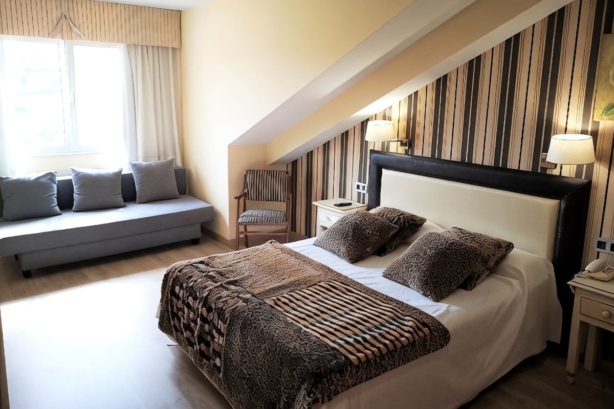 A bedroom with a large bed, a sofa, a chair, and a nightstand with a lamp.