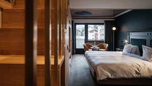 Habitación de hotel con una cama, un área de descanso con dos sillones, una mesita y vistas a edificios al exterior.