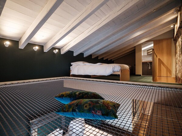 A room with a high ceiling, a bed, a small table, and a unique mesh floor.