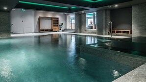 Una piscina interior moderna con vista despejada del área de la piscina, un banco de madera y una escalera que lleva a un nivel superior.