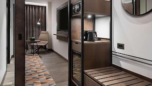 A modern hotel room with a wooden floor, a sofa, a TV, a coffee machine, and a mirror. - Serdika (Sofia)