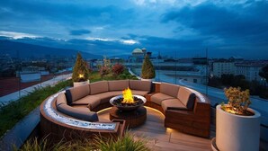A rooftop terrace with a curved seating area, a central fire feature, and potted plants. - Serdika (Sofia)
