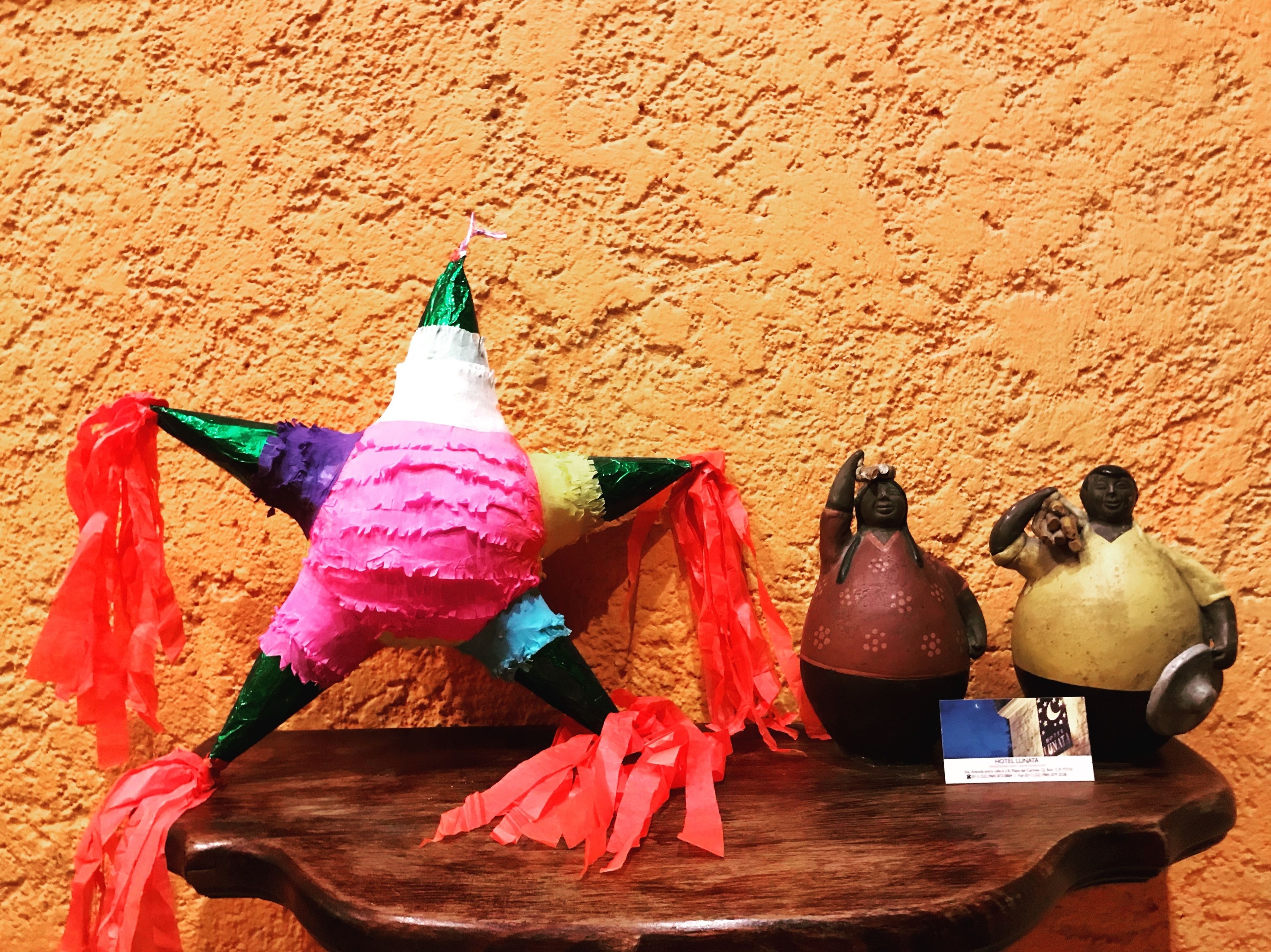 Uma mesa de madeira com uma piñata, duas figuras de cerâmica e um pequeno cartão.