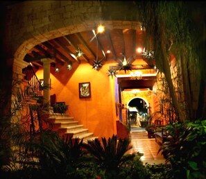 Uma escadaria leva a um espaço interior iluminado, com um arco de pedra e luzes em formato de estrela penduradas.