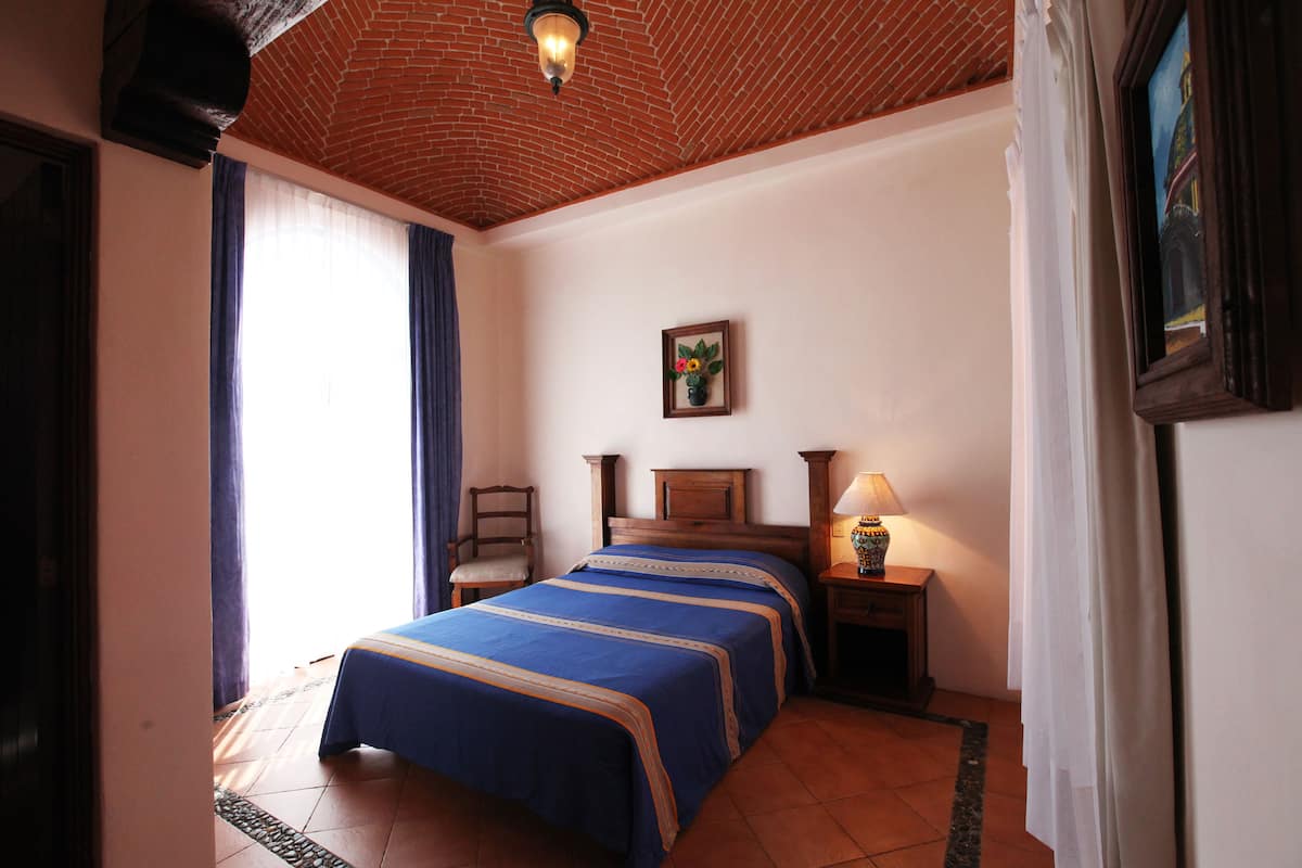 A hotel room with a double bed, a nightstand, a lamp, a framed picture, and a window with curtains.