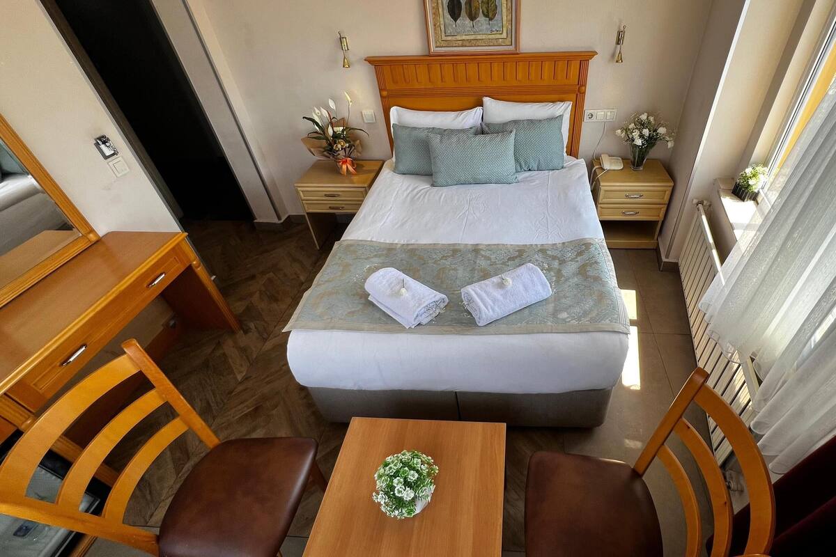A hotel room with a bed, bedside tables, a desk with chairs, and a window with curtains.