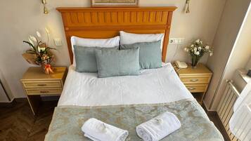 Habitación de hotel con una cama grande, dos mesitas de noche con lámparas, un cabecero de madera, una impresión botánica enmarco, una pequeña mesa con un arreglo floral y dos sillas marrones.