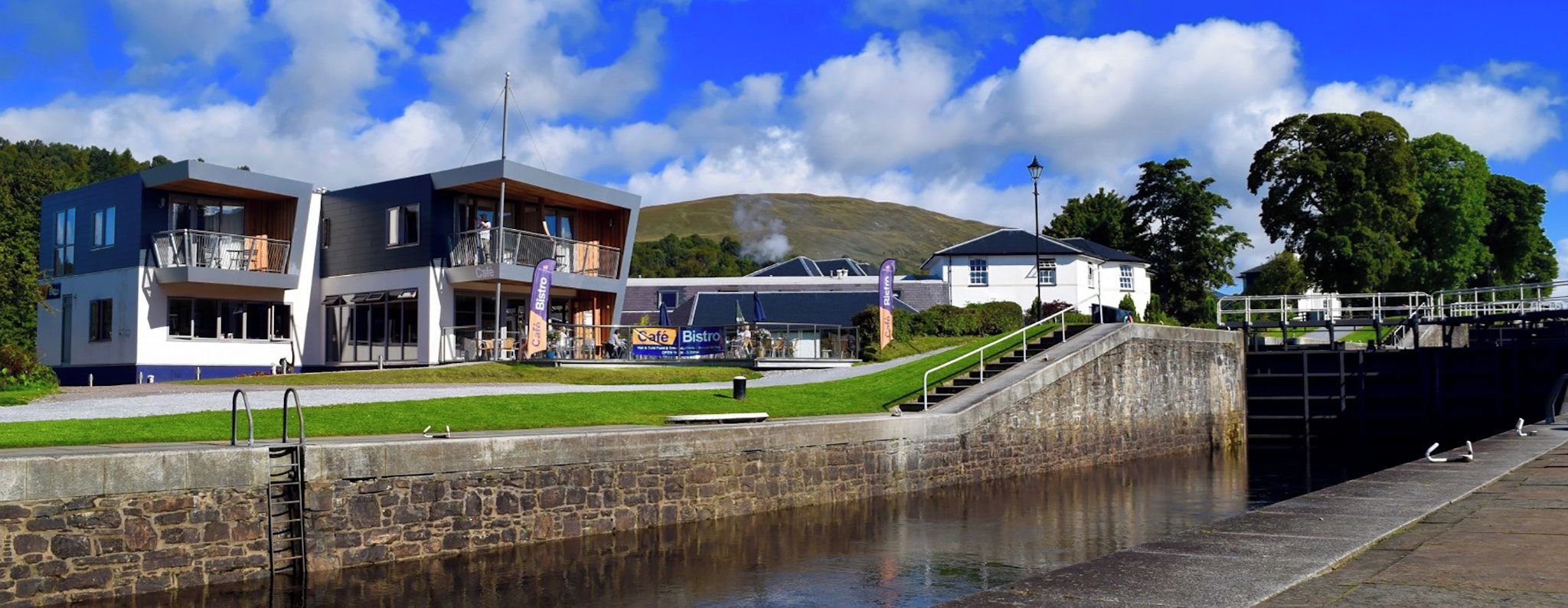 A modern building with a cafe and bistro, a stone wall, and a lock gate.