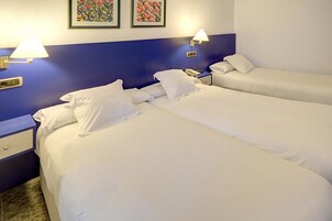 Habitación de hotel con dos camas, una mesita de noche, una lámpara y dos cuadros en la pared.