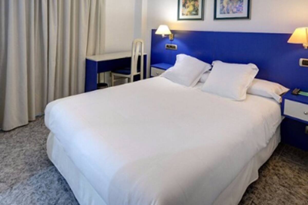 Une chambre d’hôtel avec un grand lit, deux lampes de chevet, un bureau et une chaise.