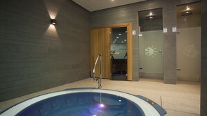 A modern indoor pool area with a clear glass wall, wooden doors, and a visible shower area. - Hotel Acuazul (Peniscola)