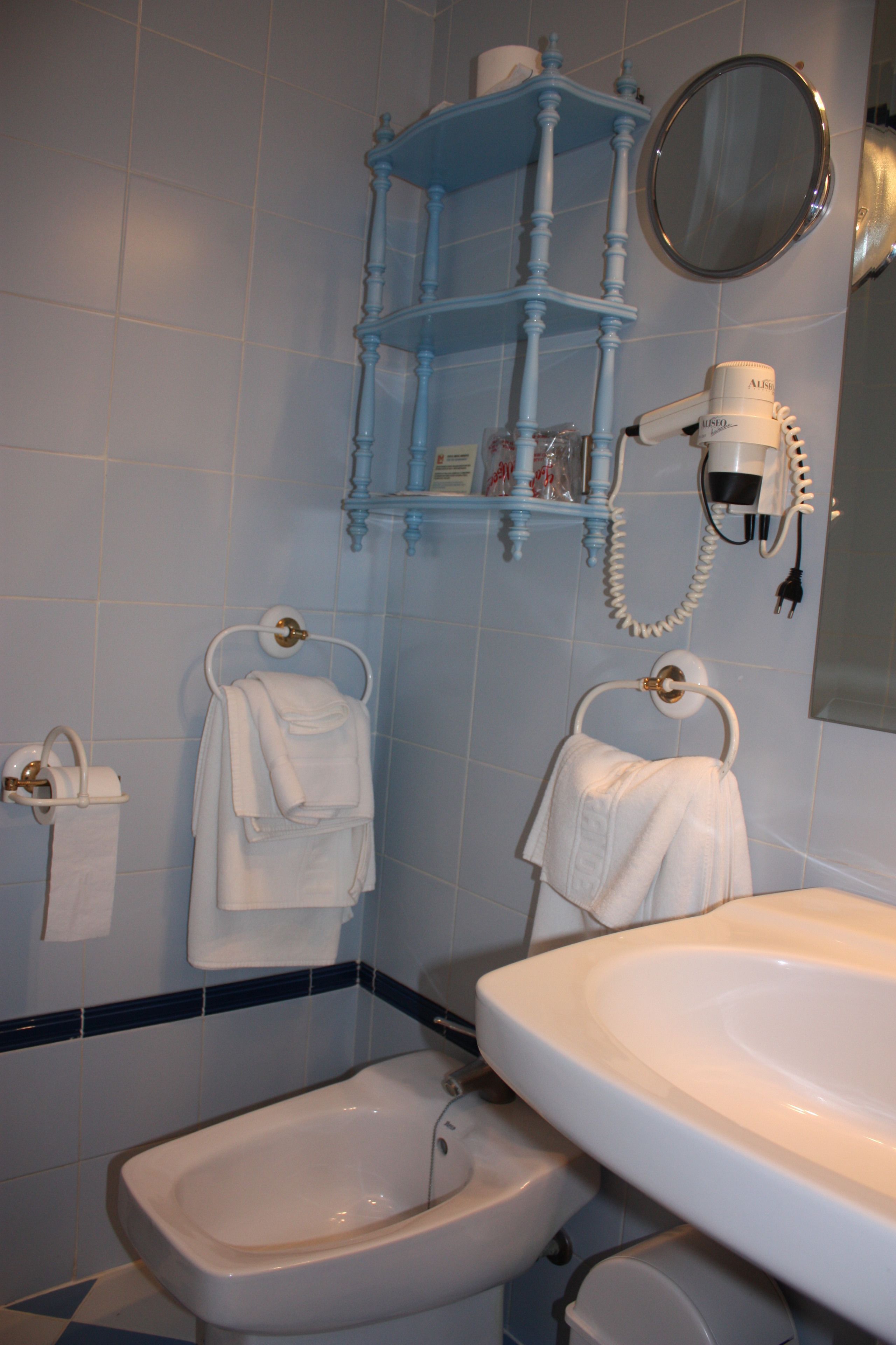 A bathroom with a white sink, a bidet, a towel rack, a mirror, and a blue cabinet.
