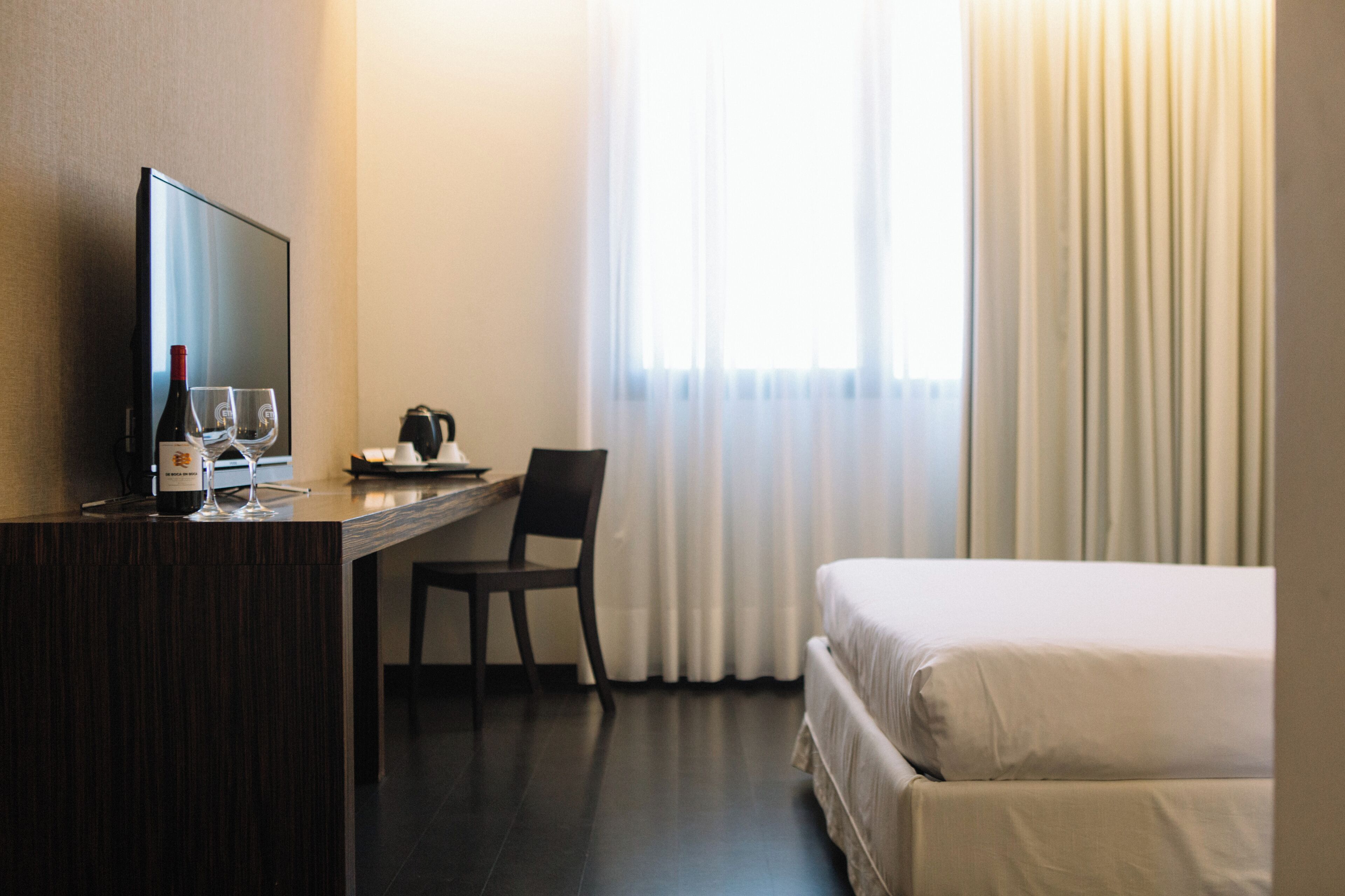 Une chambre d’hôtel avec un lit, un bureau avec une télévision, une chaise et une fenêtre avec des rideaux.