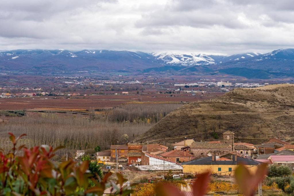 Un pueblo con edificios, una colina y montañas nevadas al fondo.