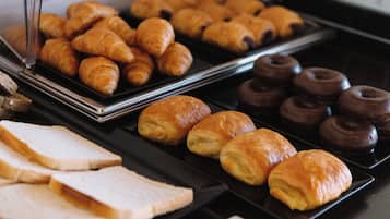 Un bufé con diversas opciones de panadería, incluyendo croissants, donuts de chocolate y rebanadas de pan.