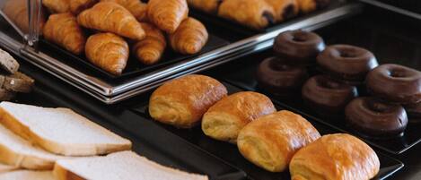 A buffet with various baked goods including croissants, chocolate donuts, and slices of bread.