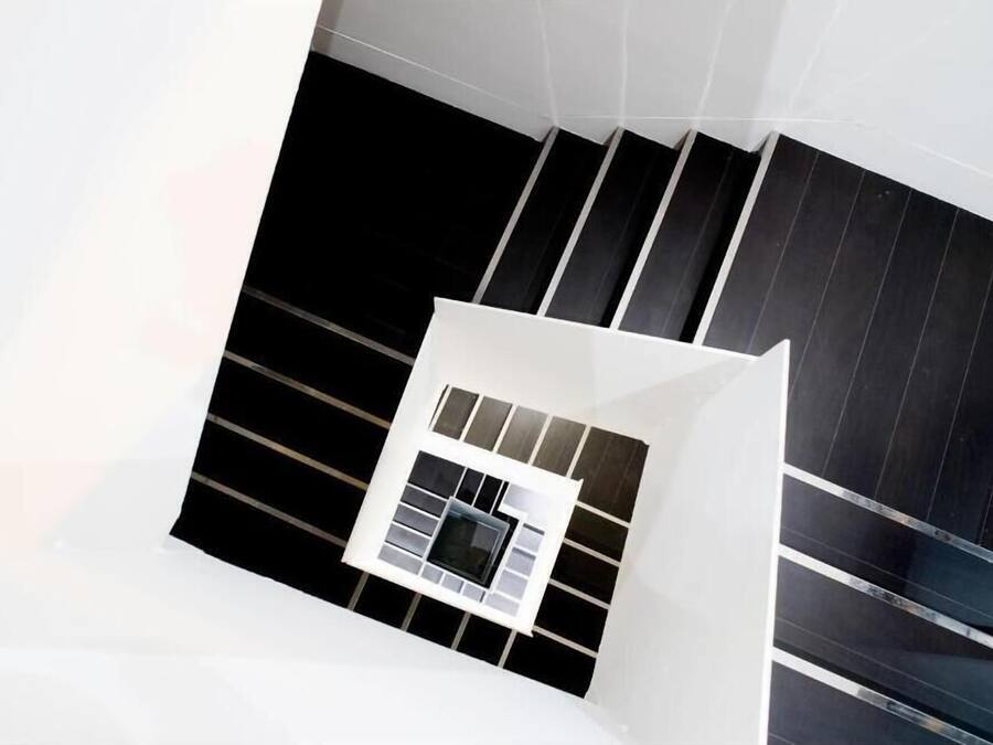 A modern staircase with black and white tiles, leading to a room with a white wall and a window with multiple panes.