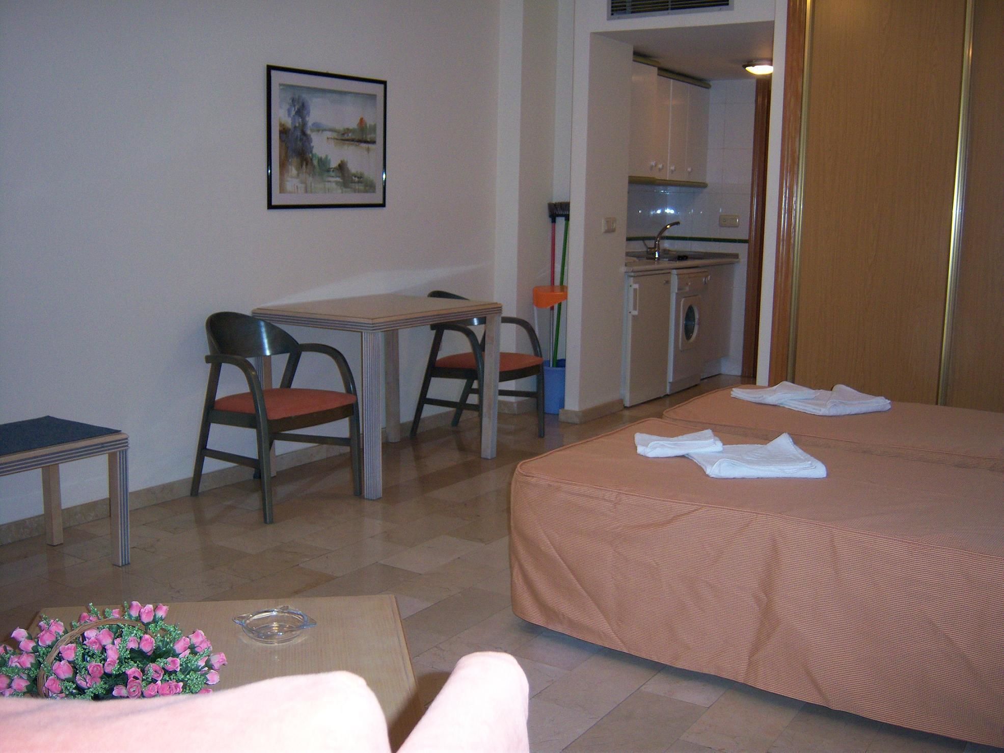 Una camera d'albergo con un letto, una scrivania con due sedie, un tavolino, un quadro appeso e un angolo cottura.