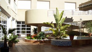 A courtyard with potted plants, a fountain, and a building with large windows and balconies. - Aguas Salinas (San Pedro del Pinatar)
