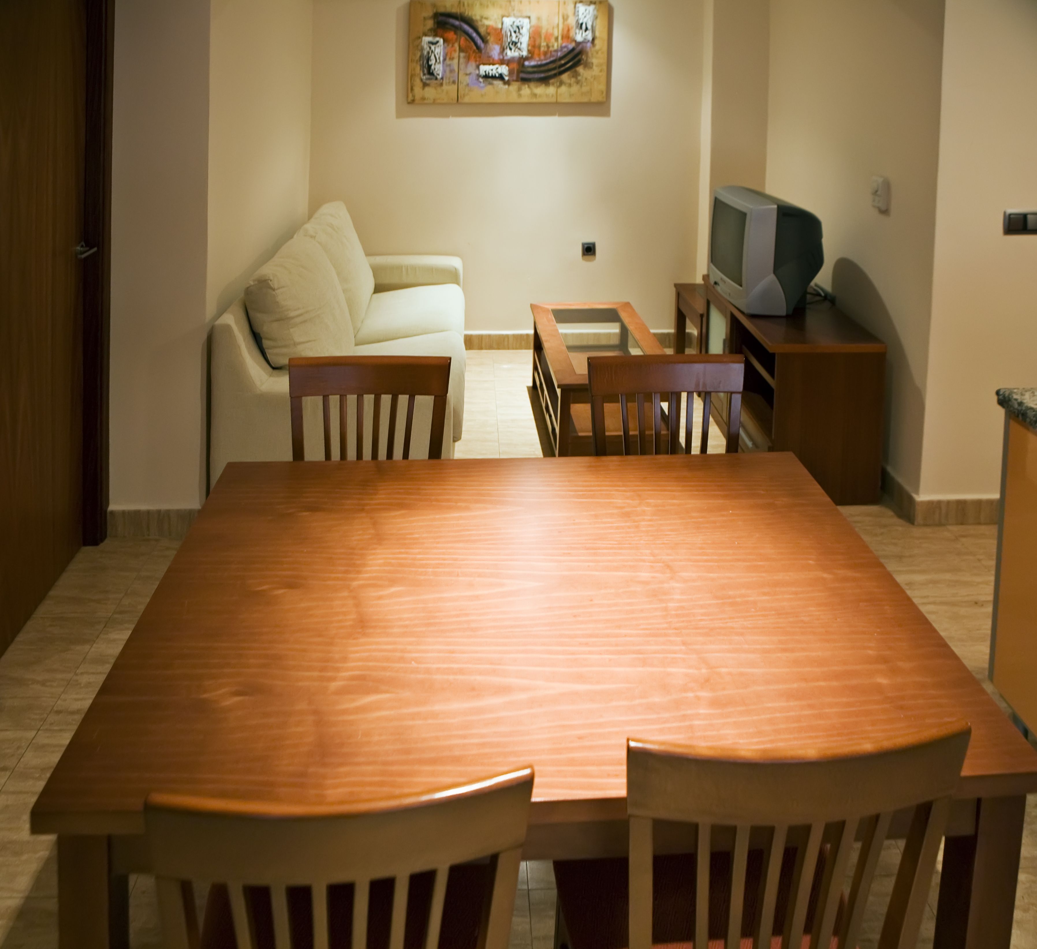 Een eetgedeelte met een houten tafel en stoelen, een bank, een televisie en een schilderij aan de muur.