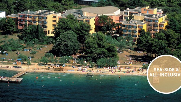 An all-inclusive resort with a sea-side view, featuring multiple buildings and a beach area.