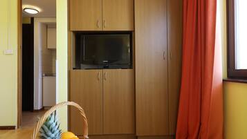 Una habitación con armarios de madera, un televisor y una cesta de fruta sobre una mesa redonda.