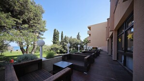 An outdoor seating area with wicker furniture and a wooden deck, overlooking a landscaped garden and a building with large windows.