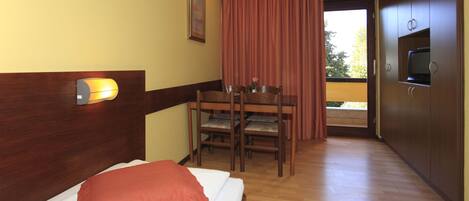 Una habitación de hotel con una cama, un escritorio con sillas, un televisor y una ventana con cortinas.