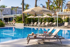 A pool area with lounge chairs, umbrellas, and palm trees.