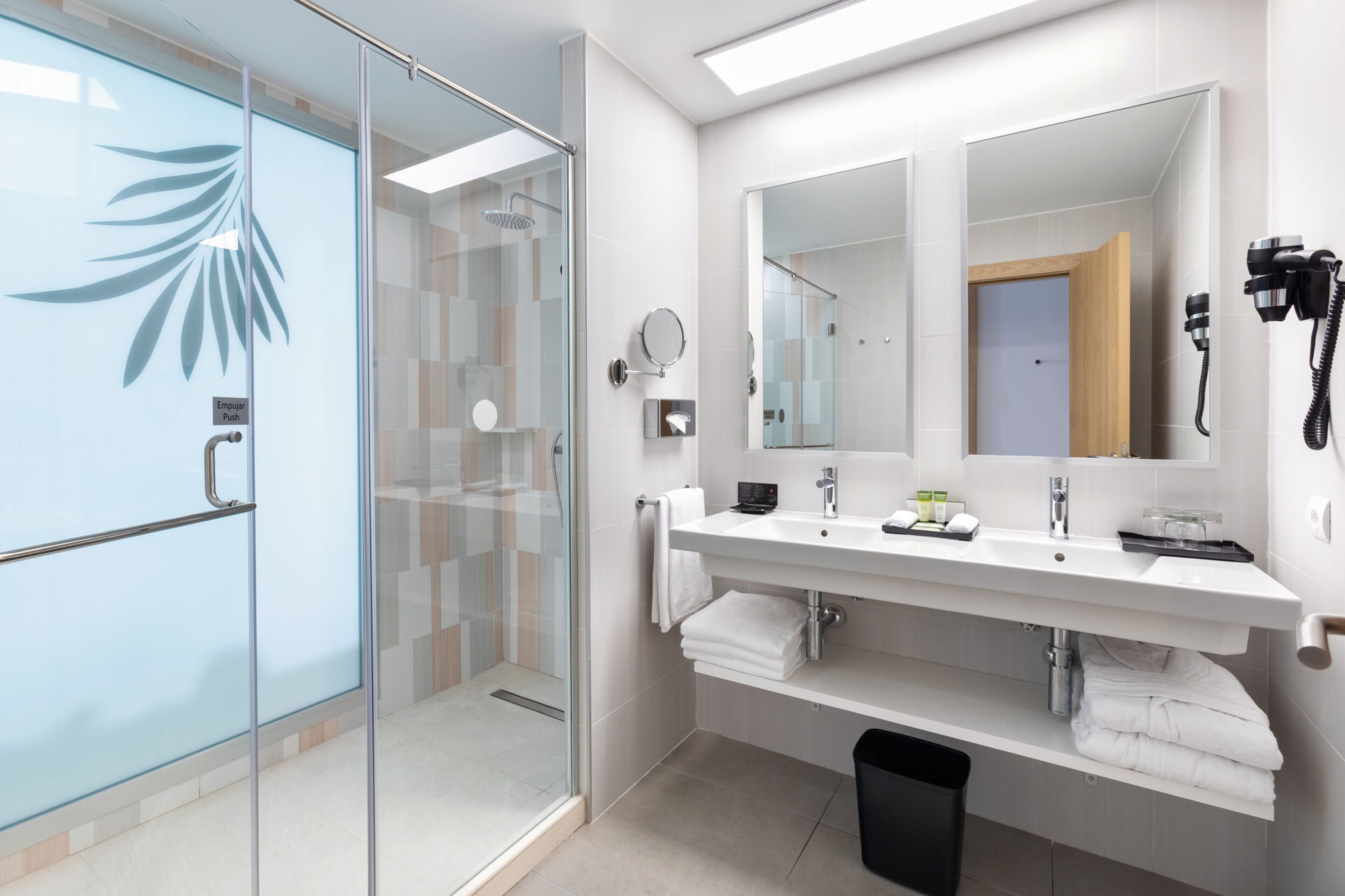 Un baño moderno con cabina de ducha de vidrio, un espejo grande y un tocador con lavabo y toallero.