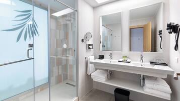 Un baño moderno con cabina de ducha de vidrio, un espejo grande y un tocador con lavabo y toallero.