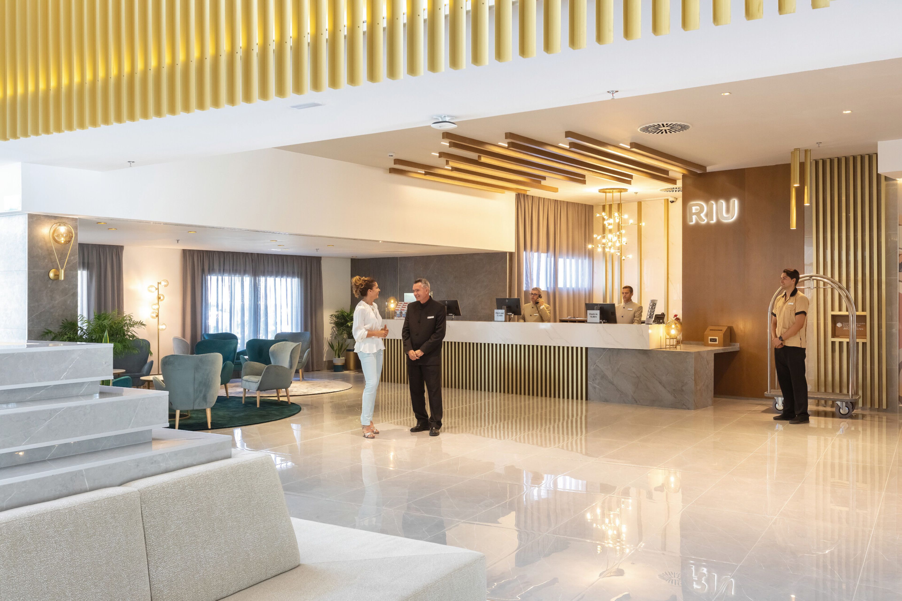 A modern hotel lobby with a reception desk, seating area, and a staircase leading to another level.