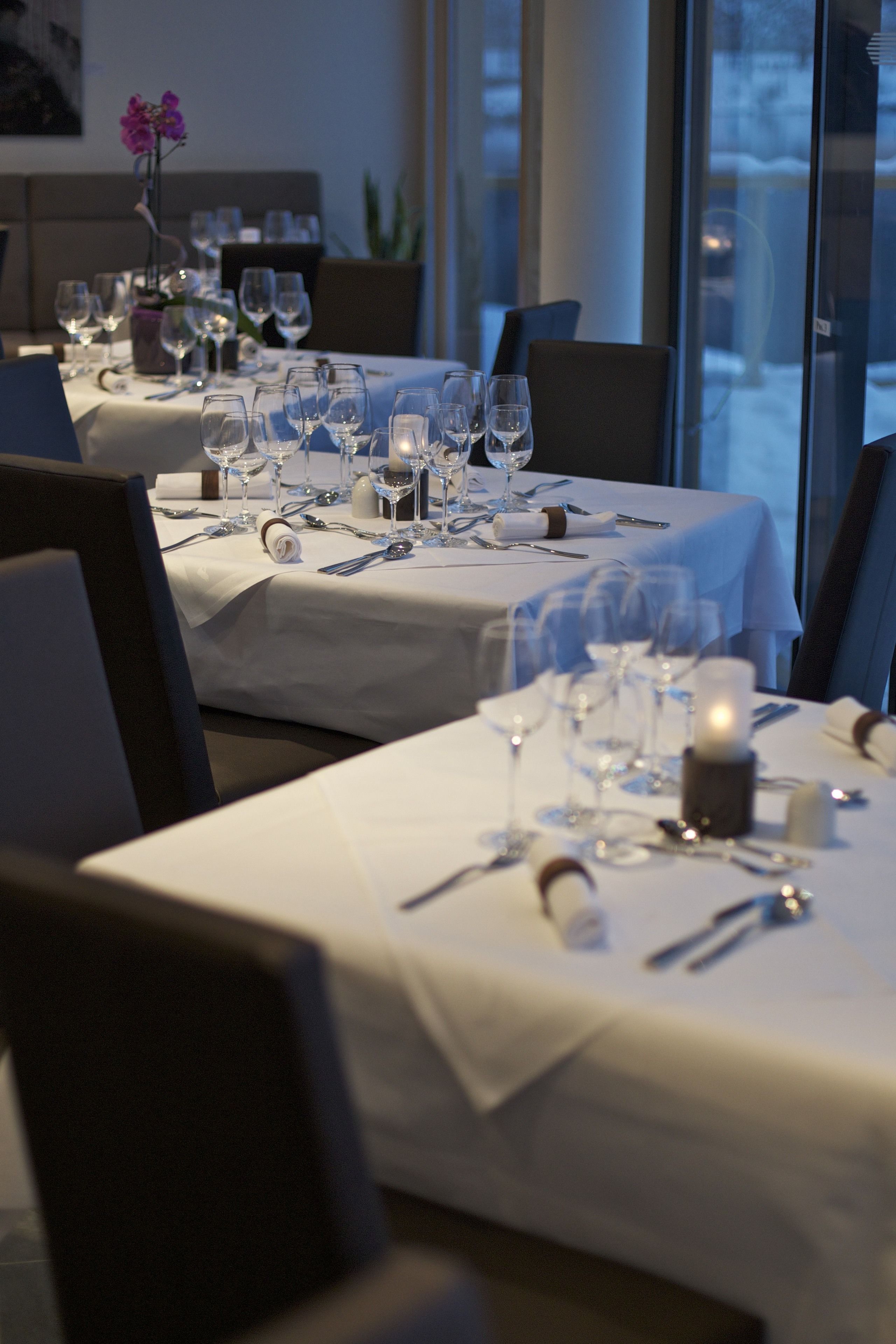 A dining area with tables set for a meal, featuring white tablecloths, wine glasses, and candles.