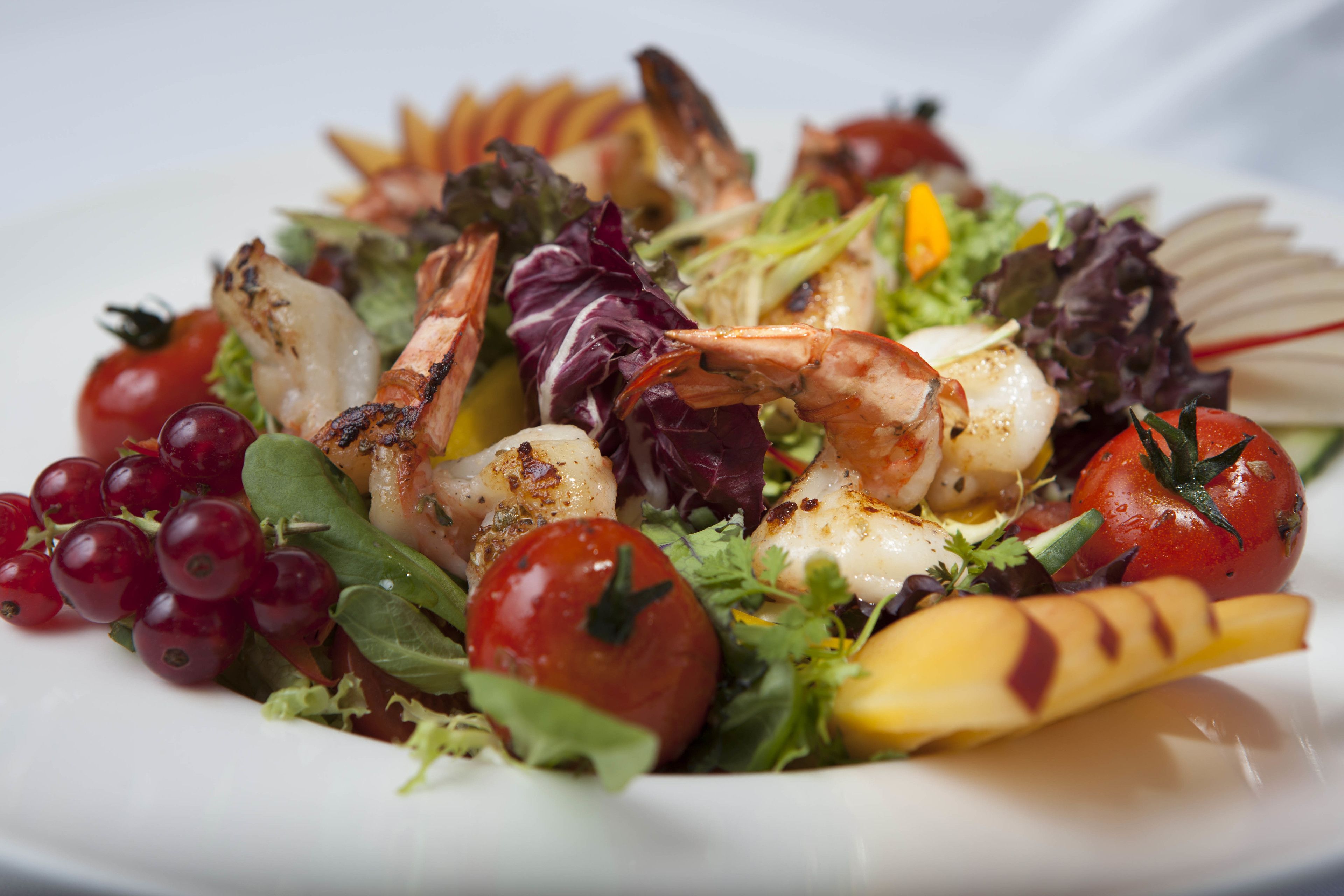 A seafood salad with shrimp, tomatoes, and greens on a white plate.