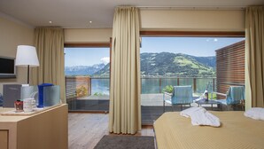 A hotel room with a bed, a desk with a lamp, a TV, and a view of mountains and water. - Seevilla Freiberg (Zell am See)