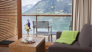 A balcony with a view of mountains and a lake, a wooden table with a vase of flowers, and a gray sofa with a green throw. - Seevilla Freiberg (Zell am See)