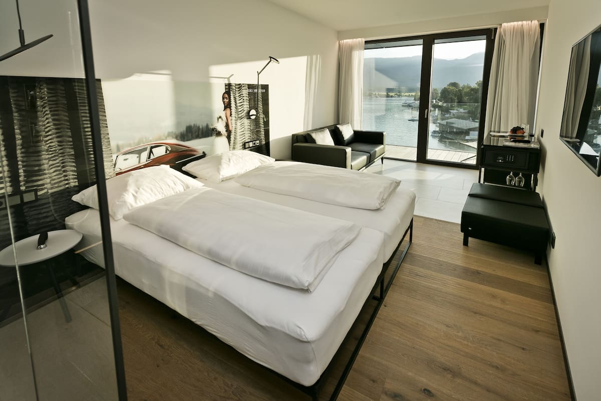 Ein modernes Hotelzimmer mit zwei Betten, einem Schreibtisch, einem Stuhl und Blick auf ein Gewässer durch große Fenster.