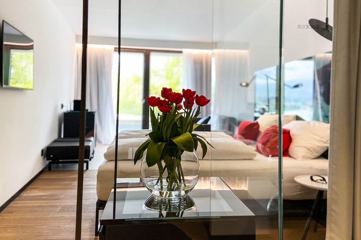 Ein modernes Hotelzimmer mit Glastisch, einem Bett mit weißer Bettwäsche und Blick ins Freie.