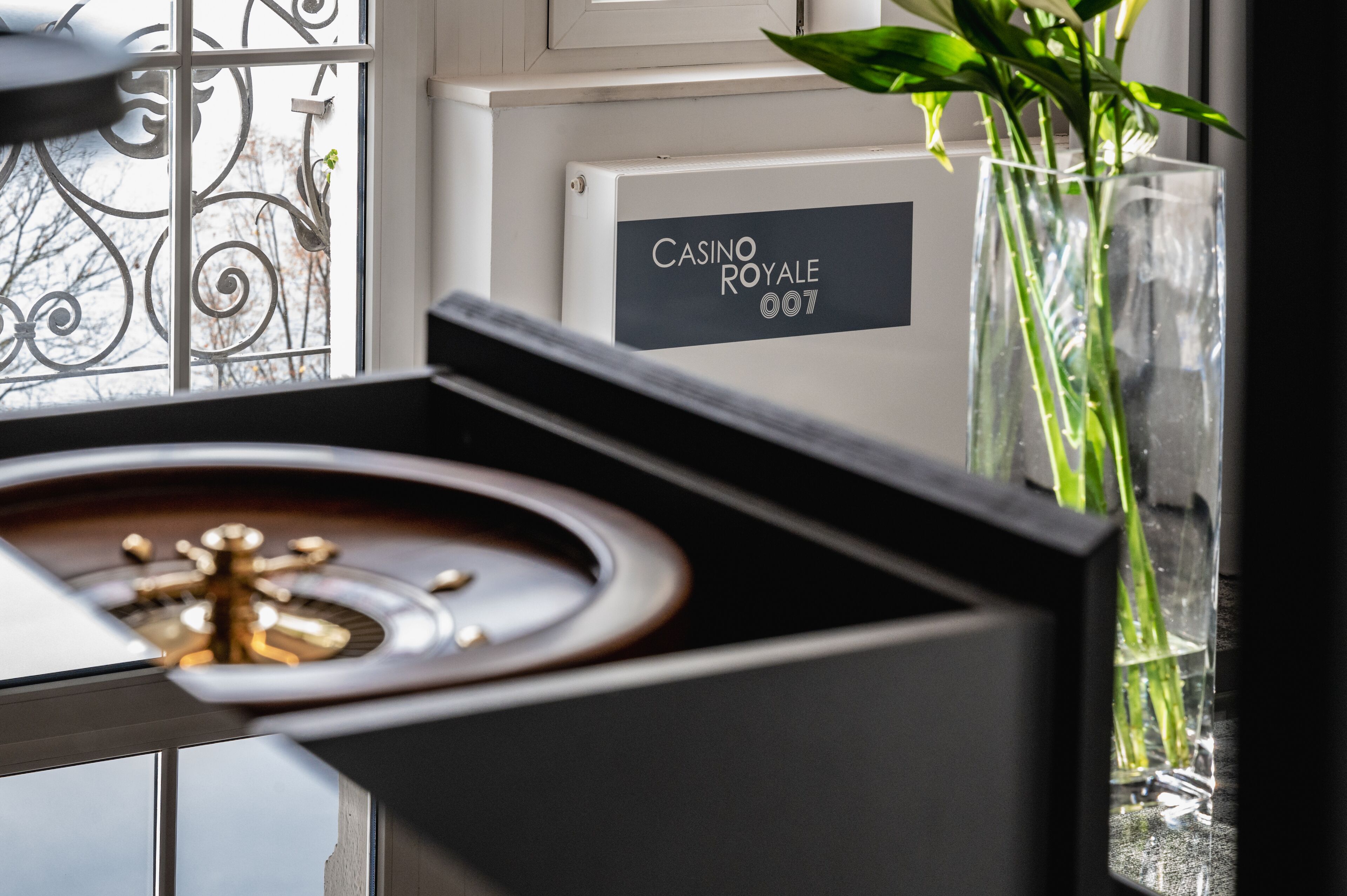 Une pièce avec un piano, une enseigne sur laquelle on peut lire « CASINO ROYALE 007 », et un vase contenant des plantes vertes.