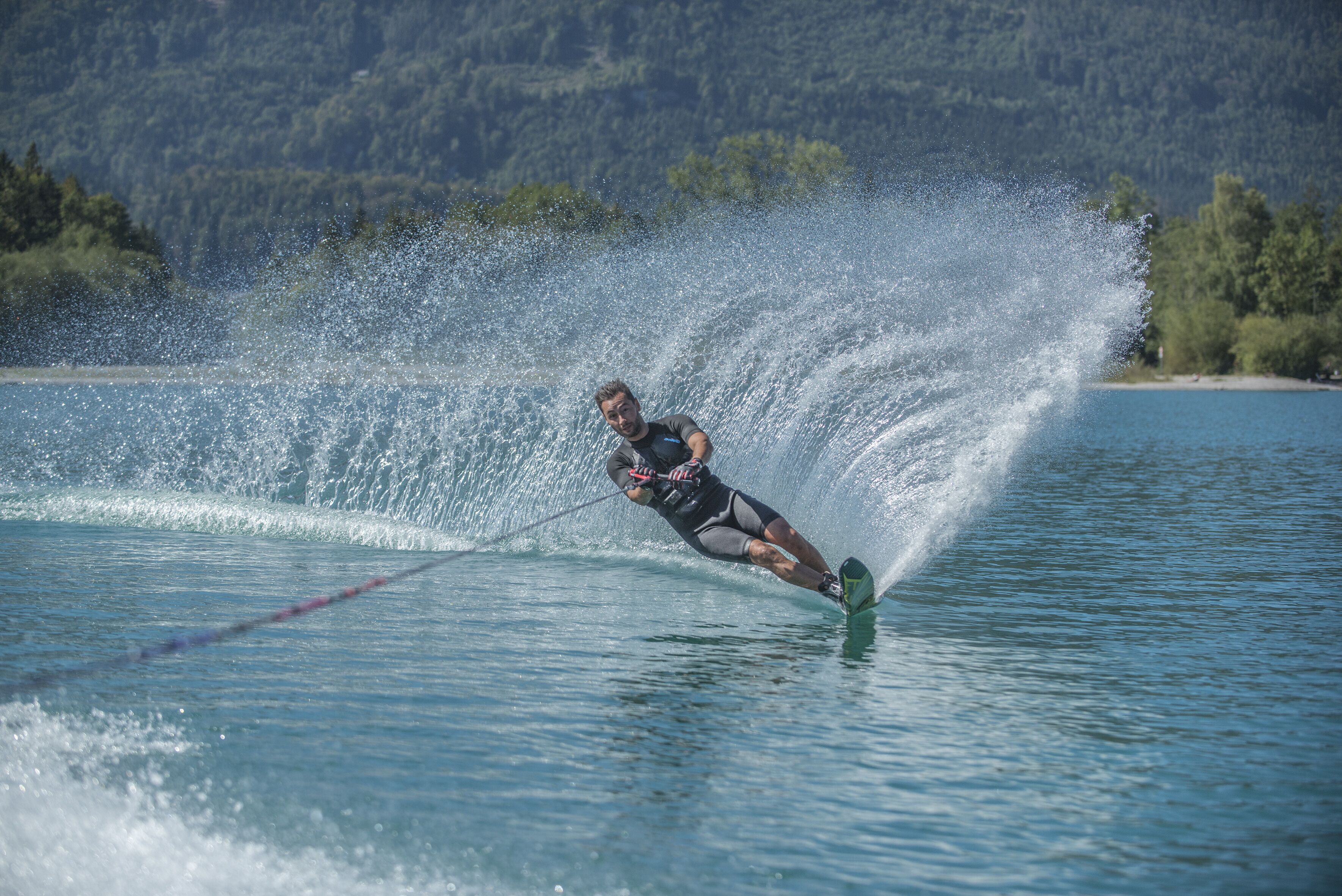A person wakeboarding on a lake with a forested mountain in the background.
