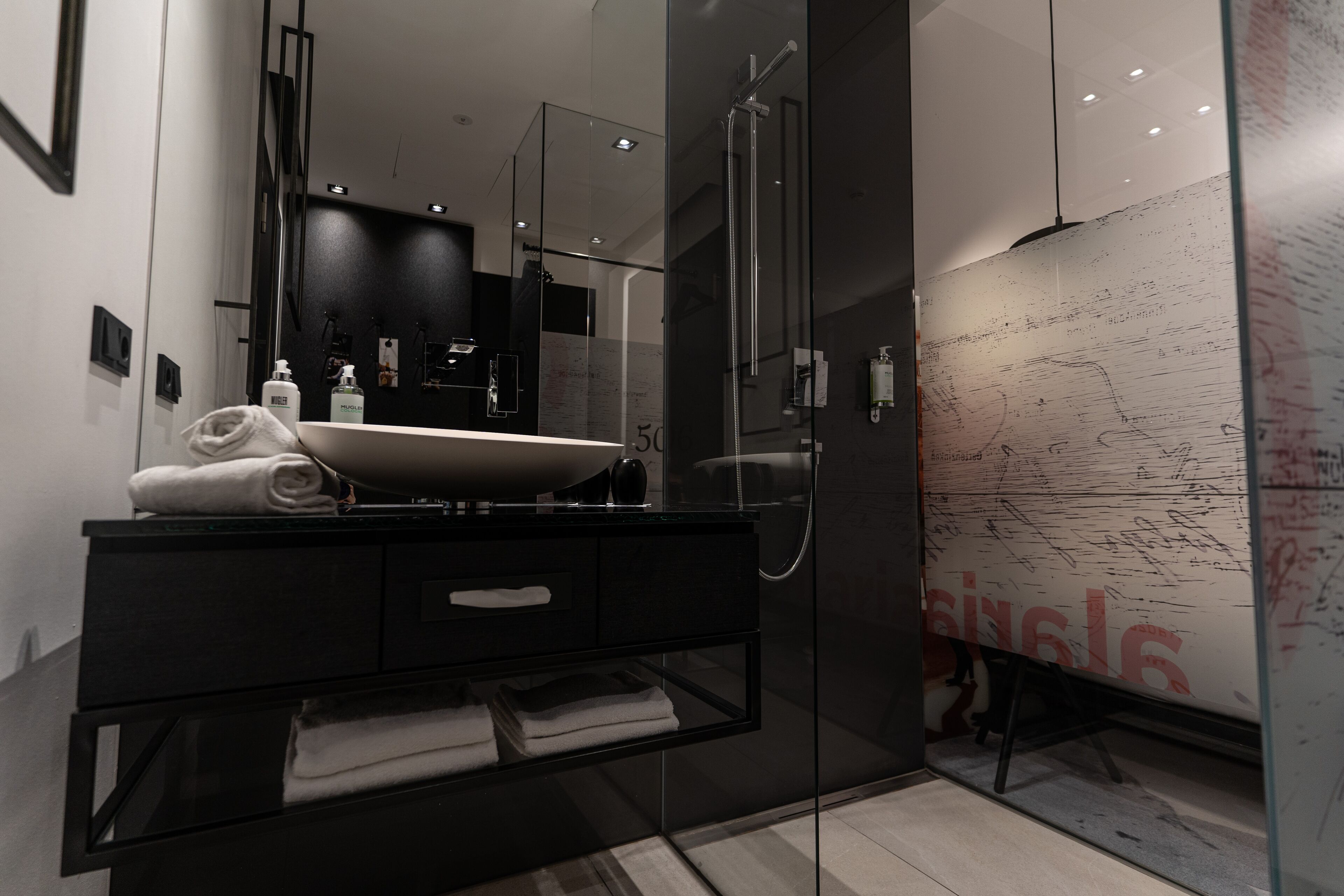 A modern bathroom with a glass-enclosed shower, a black vanity with a large mirror, and a marble floor.