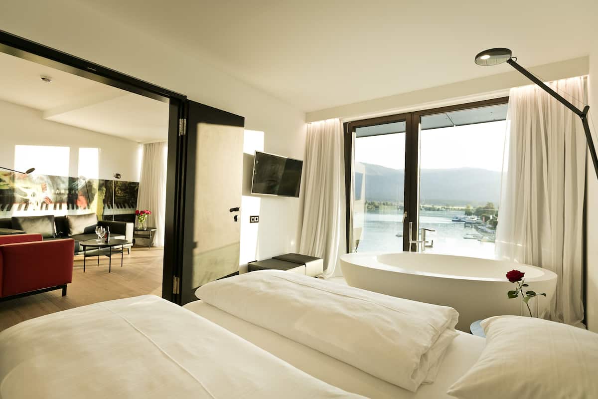 Ein modernes Hotelzimmer mit großem Fenster, einer Badewanne, einem Flachbildfernseher und einem roten Sofa.