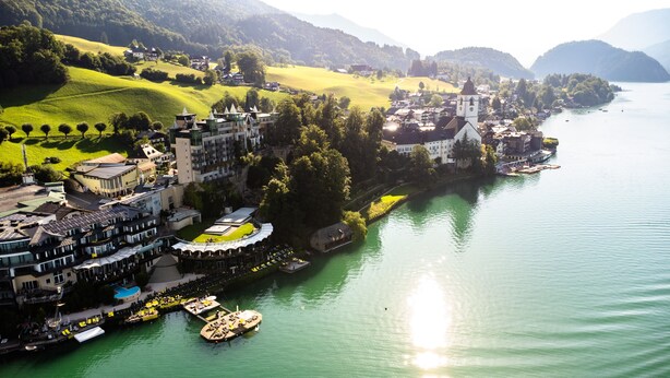 A riverside hotel with multiple buildings, a dock with boats, and a church. - Scalaria Sunset Wing (Sankt Wolfgang im Salzkammergut)