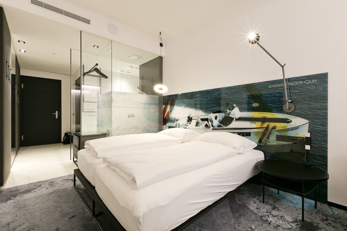 Ein modernes Hotelzimmer mit einem großen Bett, einem Schreibtisch, einem Sessel und einem Wandbild eines Bootes.