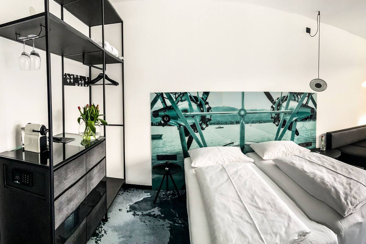 Ein modernes Hotelzimmer mit Bett, einer Sitzecke, einem großen Fenster mit Blick und einem einzigartigen Kunstwerk an der Wand.