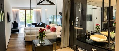 Un dormitorio moderno con una cama grande, mesita de noche y un baño con paredes de vidrio, lavamanos y espejo.