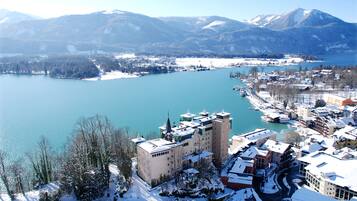 A high-altitude view of a town with a lake, snow-covered buildings, and mountains in the background.